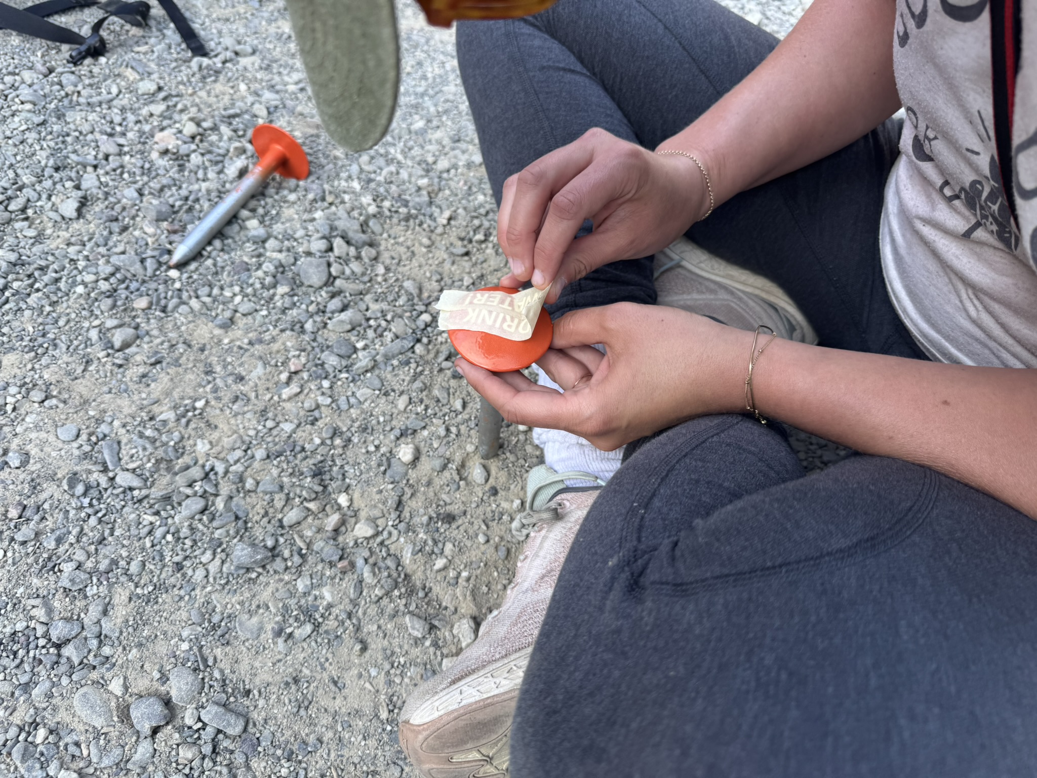 hands peeling sticker off an orange disc ground stake